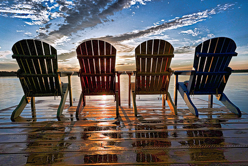 Image taken by Craig Jackson of four Adirondack chairs on a dock at sunset.